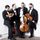 Four men in tuxedos are posing for a picture with their instruments.